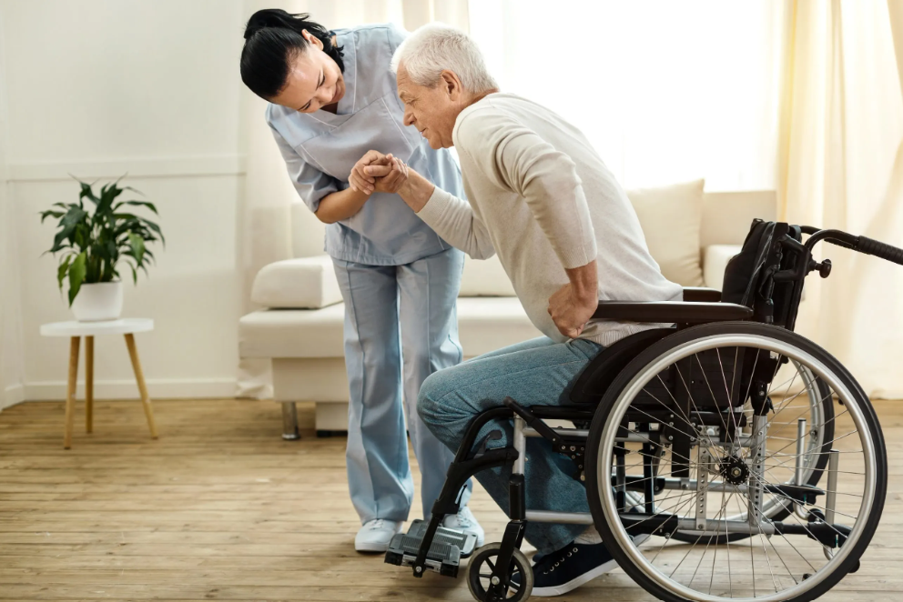 A BellMe caregiver helping an elderly man from his wheelchair at home after pressing his wireless panic button